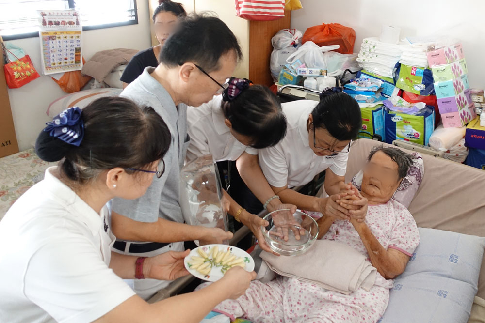 Volunteers and medical staff carrying the lucite Buddha statue, fragrant water and flowers to Madam Tan to allow her to perform the Buddha Bathing ritual.